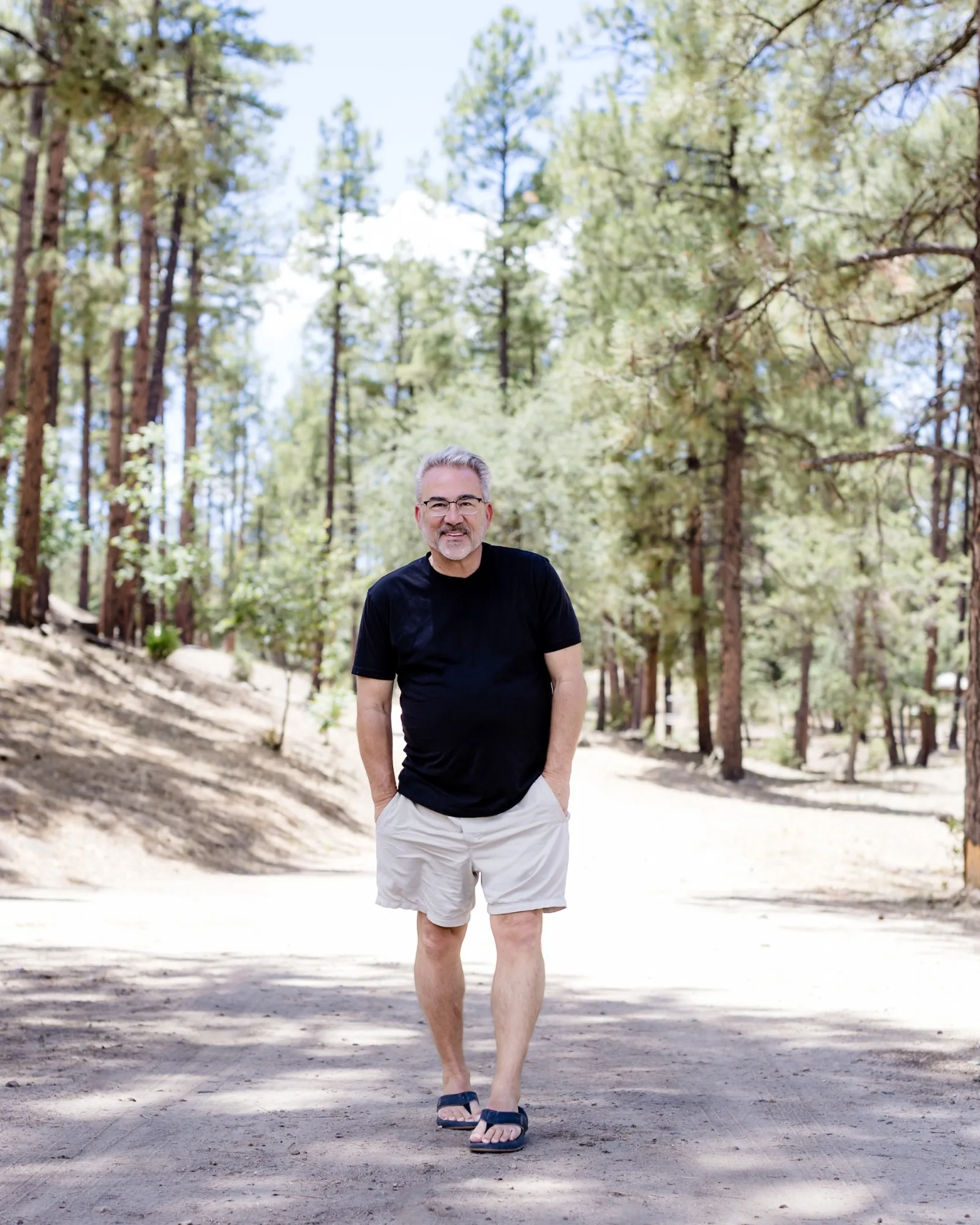 Mark P. Fisher walking along a pine-lined path, smiling toward the camera